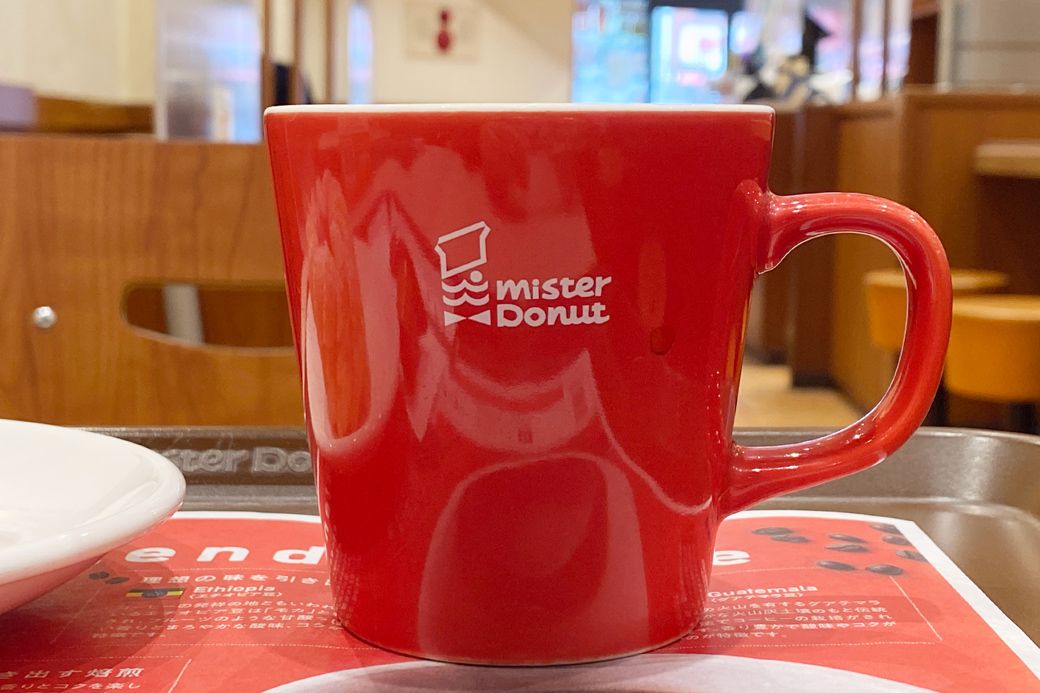 ロゴ入りのマグカップに注がれたミスド ブレンドコーヒー。マグカップは厚みとまるみのあるぽってりしたデザイン（筆者撮影）