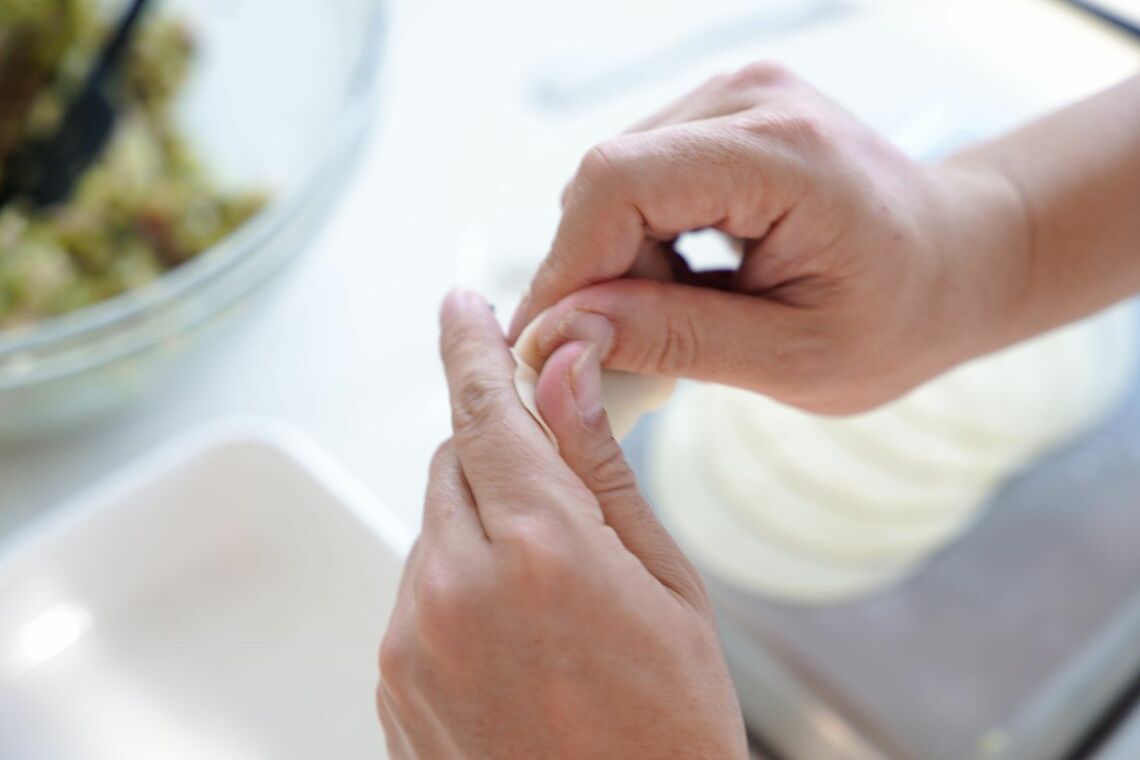 親指と人差し指で餃子の皮の縁をギュッと押さえて、皮を閉じます