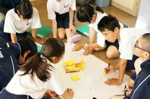 床で模造紙を広げて熱く議論する中高生たち