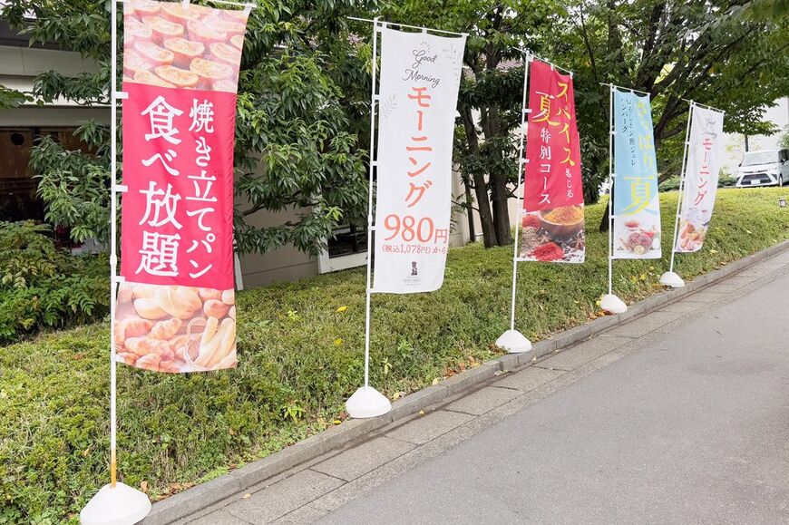店頭の植栽沿いに「焼きたてパン食べ放題」「モーニング980円」ののぼりが並ぶ（筆者撮影）