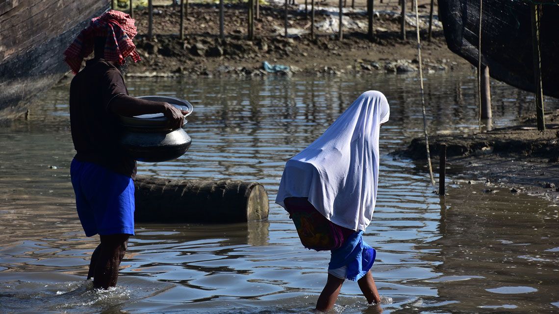 バングラデシュのコックスバザール 冠水した道路を歩くイスラム教徒の女学生と働く男性