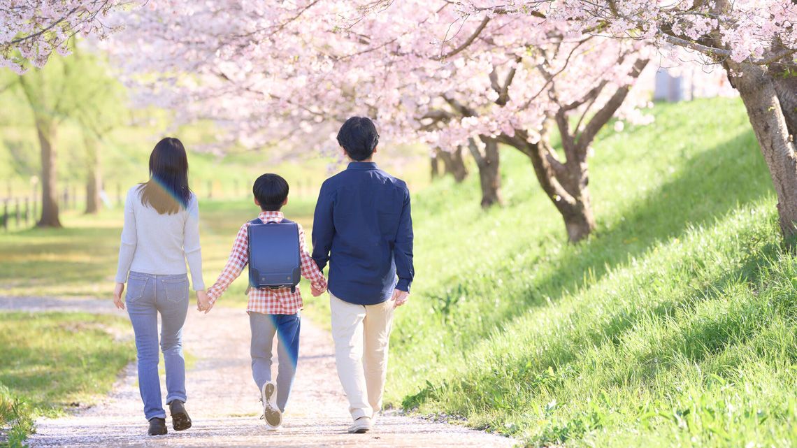 桜の咲く道を歩く親子の後ろ姿