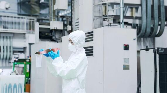 半導体工場でシリコンウエハーを検査する防護服を着た女性作業員