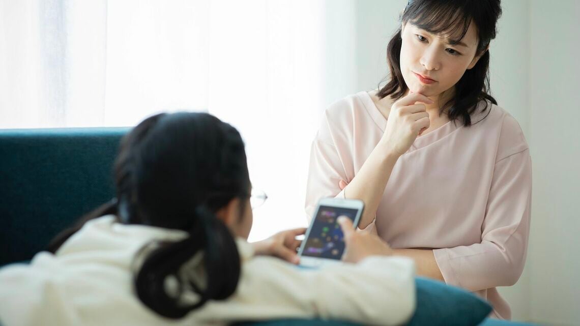 スマートフォンでゲームをする女の子と、見つめる母親