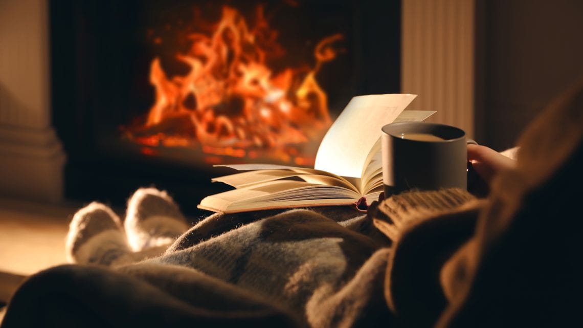 暖炉の前でカップを片手に読書する様子