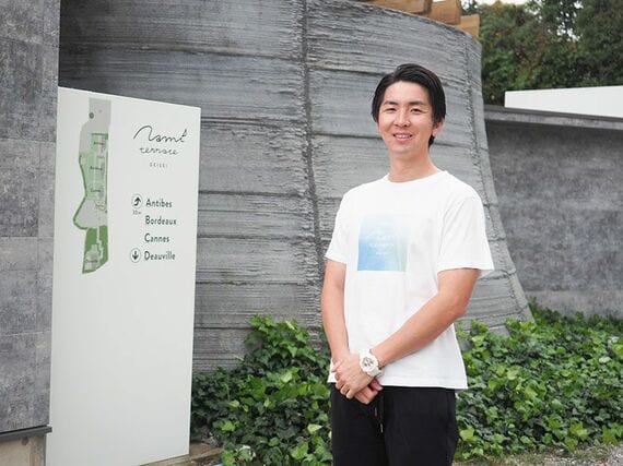 ナミテラス芸西の施工・運営管理を行う和建設の中岡竜太郎さん。バックにあるのがサウナ棟の「サウナメランジュ」の外壁（写真撮影／藤川満）