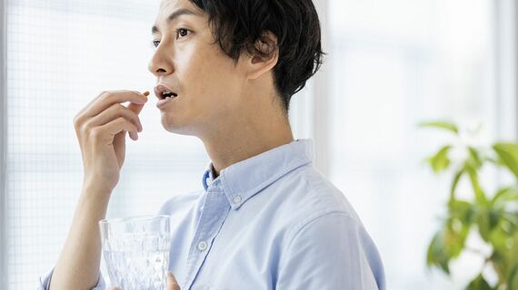 カプセル剤を水で飲もうとする男性