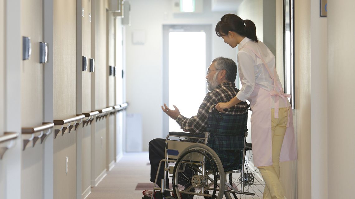 施設内で高齢者が乗る車椅子を押す看護師