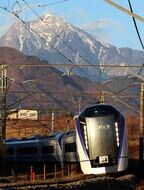 夕陽差す山並みをバックに走るE353系