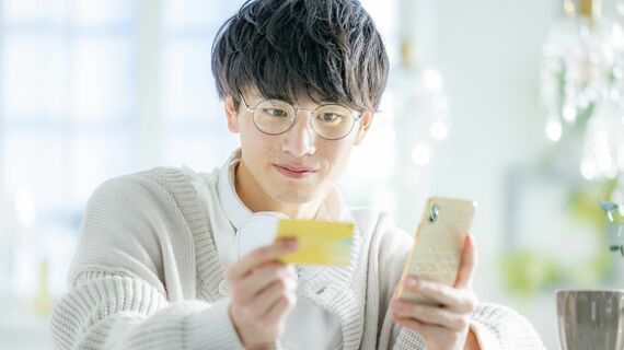 スマホとクレジットカードを見る若い男性