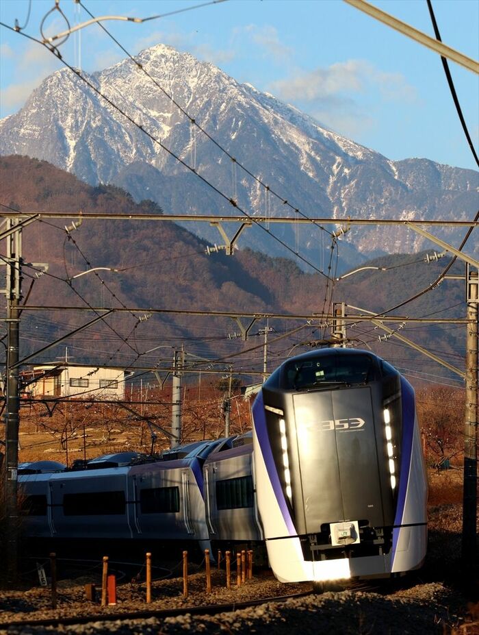 夕陽差す山並みをバックに走るE353系