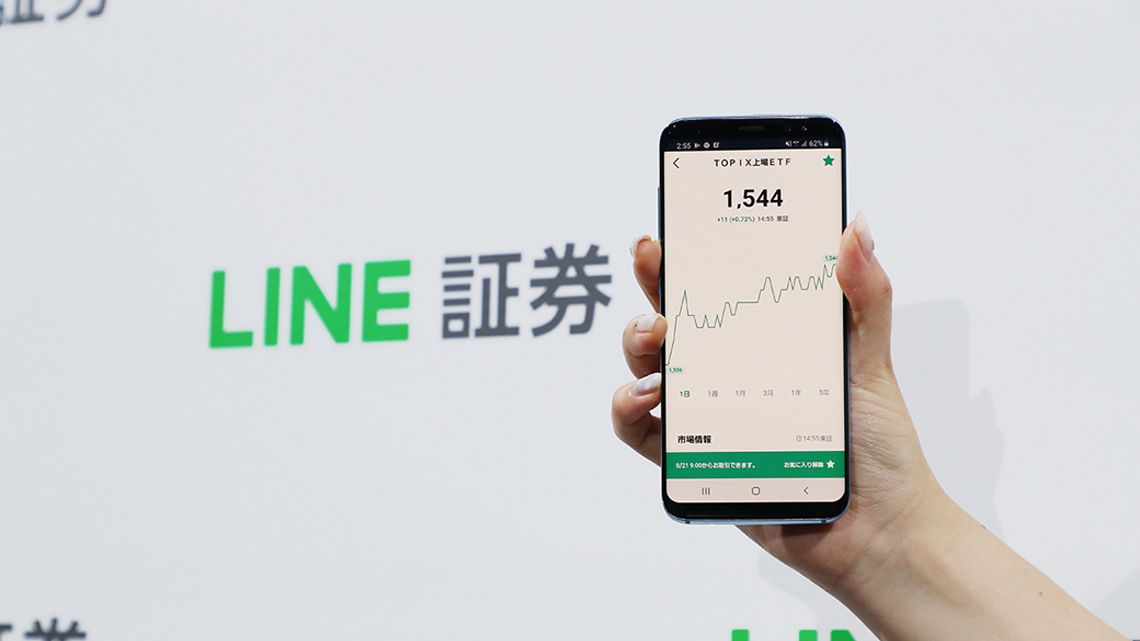 LINE証券のロゴパネルとサービス画面が映るスマートフォン