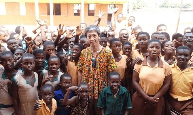 学校の中庭に集まる村の子どもたちと土居さん（写真：明治）