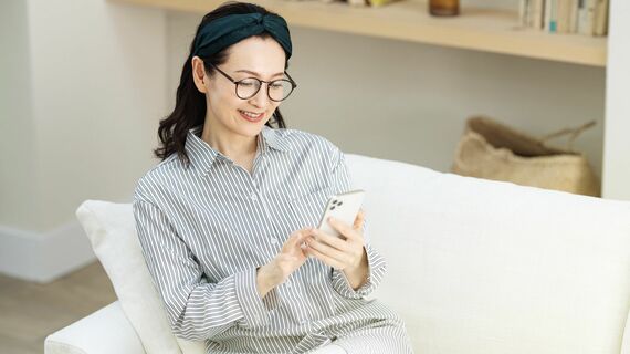 家のソファーでスマホを見るミドル女性