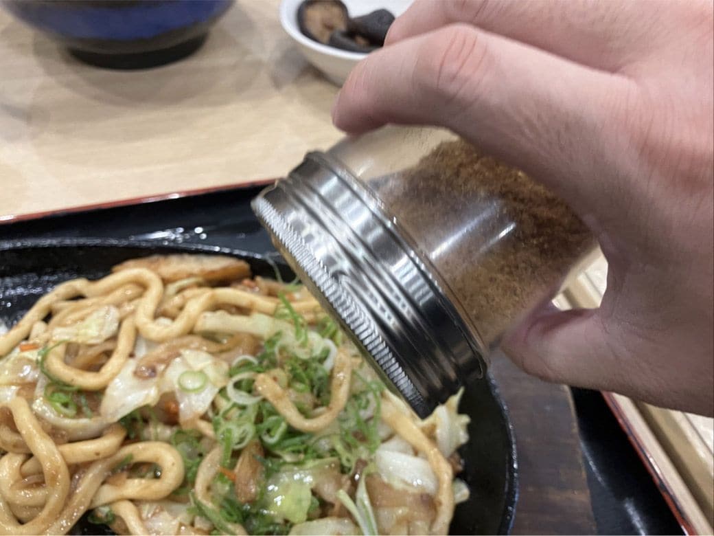 焼きうどんにふりかけをかける様子