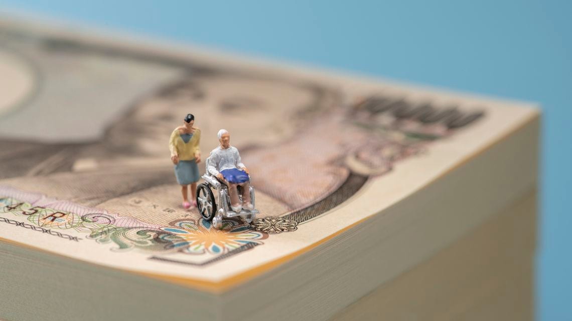 1万円札と車椅子の高齢者と介護者のミニチュア