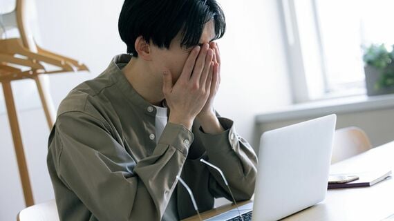 ノートPCの前で顔を覆い隠す男性