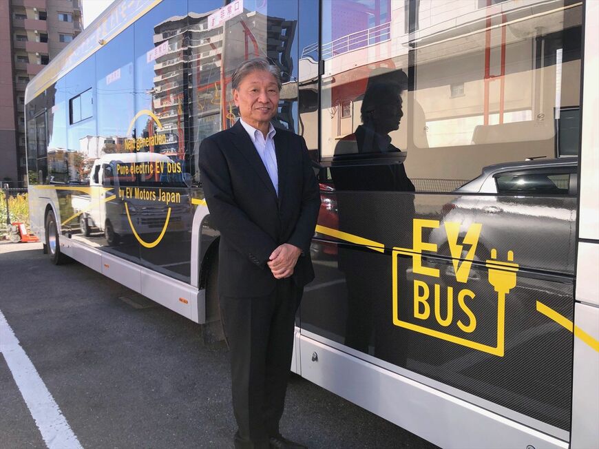 EVモーターズ・ジャパン本社内にあるEVバスの前にて佐藤氏（筆者撮影）