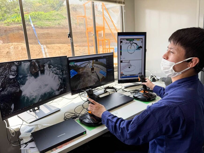 ゲーム用のジョイスティック2本とモニター3台で遠隔操作する巴山建設のスタッフ
