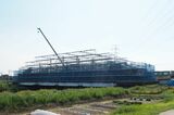 古利根川橋梁の架け替え工事の現場。手前に見えるのは新しい橋桁を造る作業構台で、後ろを列車が通っている（記者撮影）