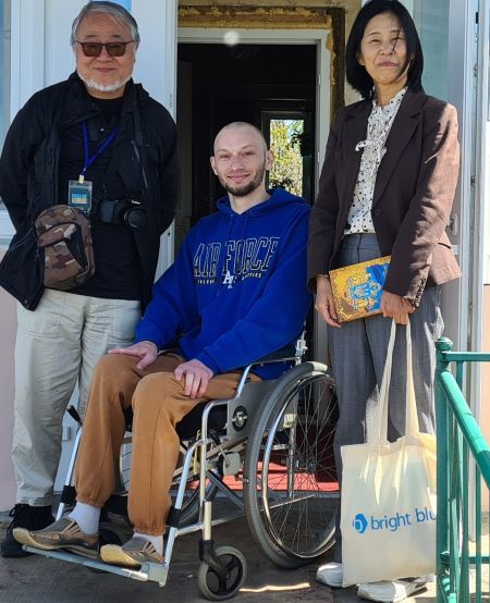 日本の車いすが届けられ、笑顔を見せるローマンさん（中央）。左が筆者、右が妻の史子（2023年5月、キーウ近郊イバンキフ村で撮影）