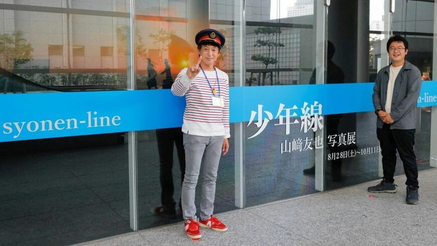 写真展会場前に立つ鉄道カメラマンの山崎友也氏（左）と村上悠太氏（撮影：村上悠太）この記事の画像を見る(◯枚)