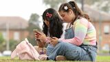オーストラリアのシドニーに住むアイリス・トルソンさん(15)は、若者の交流サイト(SNS)利用を禁止する法律が施行されて初めての夏休みに入っても、最初は家族と過ごせるからあまり問題はないだろうと考えている。写真は携帯電話を使うトルソンさんとアニエ・ワンさん。シドニーで10日撮影(2025年 ロイター/Hollie Adams)