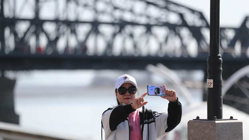 北朝鮮と国境を接する中国・丹東市で、北朝鮮と通じる橋を背景に写真を撮る中国人観光客（写真・Yu Haiyang／China News Service via Getty Images）